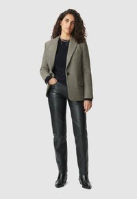 Blazer a scacchi bianco e nero con rever, indossato sopra un maglione scuro, abbinato a pantaloni di pelle neri aderenti e stivali alla caviglia.