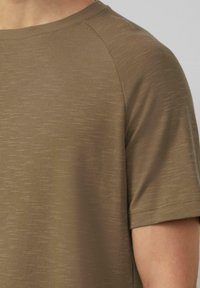 Oliwkowa, krótko-sleeve koszulka z fakturowanej tkaniny, z okrągłym dekoltem i rękawami raglanowymi. Widoczne akcenty przeszycia na rękawach.