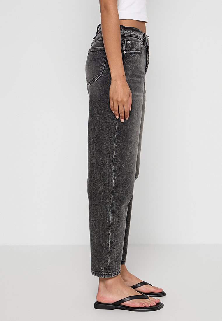 Jeans neri a vita alta con gamba dritta e texture sbiadita, design a cinque tasche e chiusura frontale con bottone, abbinati a ciabatte nere.