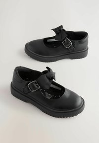 Zapatos Mary Jane negros hechos de cuero sintético texturizado, con una correa con hebilla y un detalle de lazo, sobre una suela de goma.