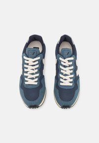 Navy blue sneaker with mesh fabric, suede accents, and cream laces. Features a textured sole and logo tag on the tongue.