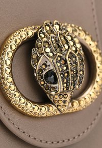 Borsa beige con una chiusura metallica dorata decorata con pietre ornamentali, tra cui accenti neri e dorati, che creano un motivo testurizzato.