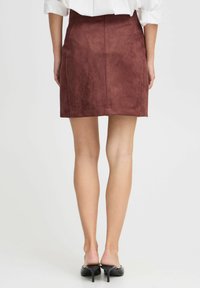 Bordeauxfarbene Wildleder-Minirock mit taillierter Passform, glatter Textur und dezenten Nähten, kombiniert mit schwarzen High Heels.