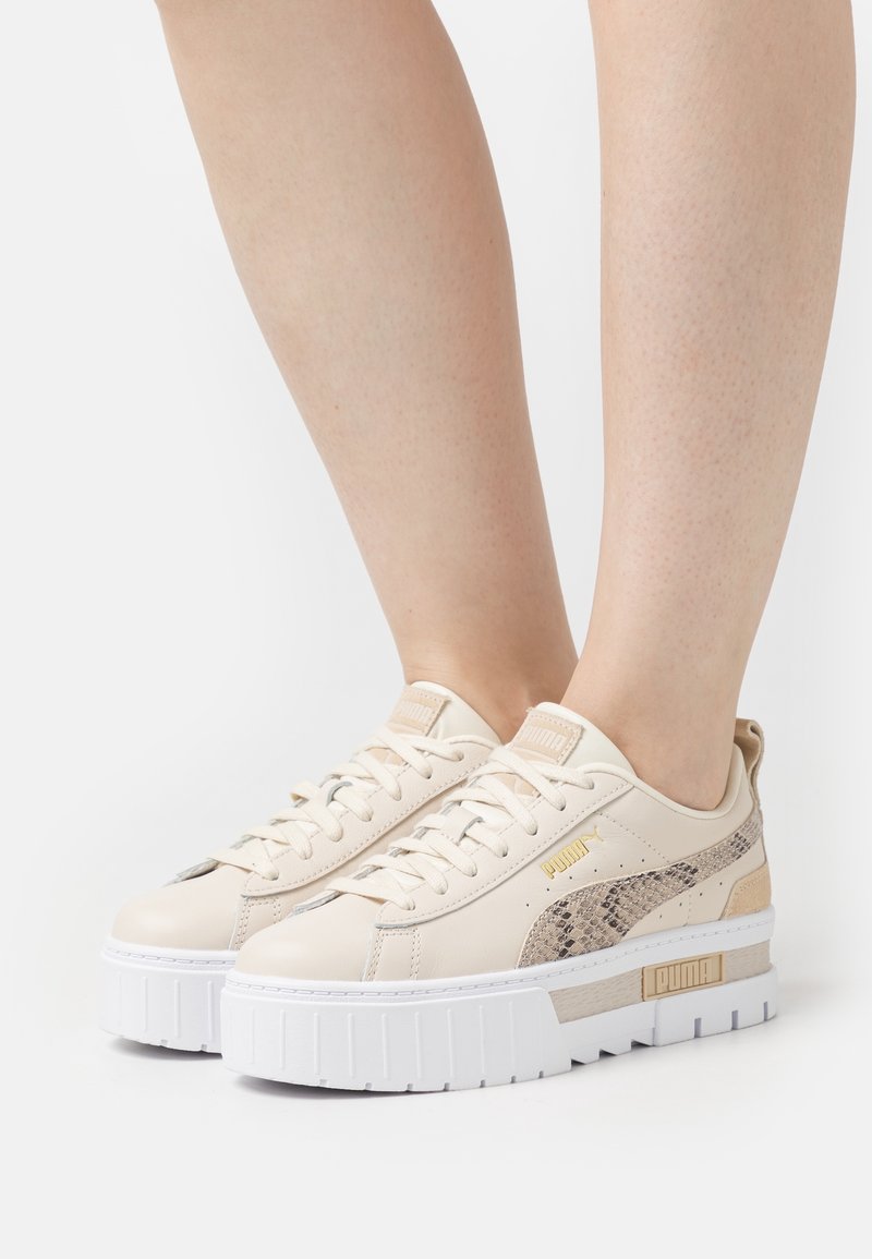 Baskets à plateforme beige Puma avec détail imprimé serpent, portées sur jambes nues, avec des semelles blanches épaisses rainurées et un design à lacets.