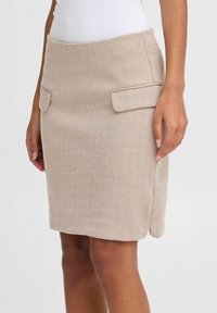 Jupe beige à motif chevrons avec une coupe ajustée, deux poches rectangulaires à l'avant et un ourlet droit. Fabriquée en tissu texturé.