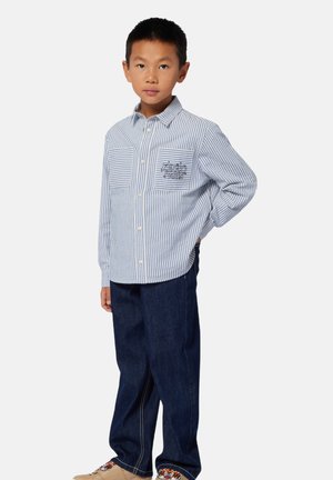 Gestreept shirt met lange mouwen in blauw en wit, met een voorzak met geborduurde tekst, gecombineerd met donkerdenim broek en lichte schoenen.