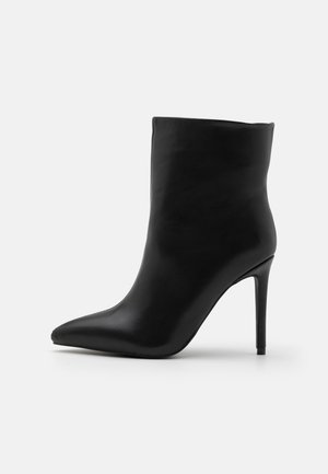 Bottine en cuir noir à bout pointu avec talon stiletto fin, finition lisse et tige de hauteur moyenne sur fond uni.