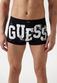 Črne bokserice s prilagojeno obliko. Imajo izrazit bel logotip "GUESS", vzorec škropljenja in elastičen pas z logotipom.