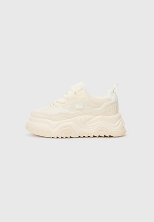 Cream-colored chunky sneaker with thick wavy sole, lace-up front, pull tab at heel, and subtle textured detailing on upper and sole.