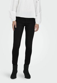 Jeans ajustados negros con una textura suave, combinados con botines de ante negros con un patrón geométrico, llevados con una blusa blanca.