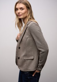 Szary teksturowany blezer z dwoma guzikami, jedną kieszenią na piersi oraz dwoma przednimi kieszeniami. Założony na niebieskie dżinsy, widoczny pod lekkim kątem.