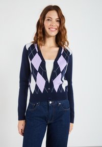 Marineblå strikket cardigan med V-hals, knapper og et diamantmønster i lilla og hvit over fronten.