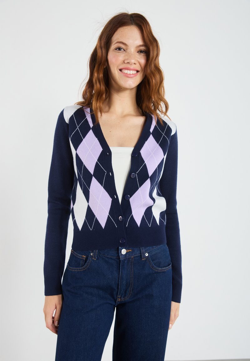 Marineblå strikket cardigan med V-hals, knapper og et diamantmønster i lilla og hvit over fronten.