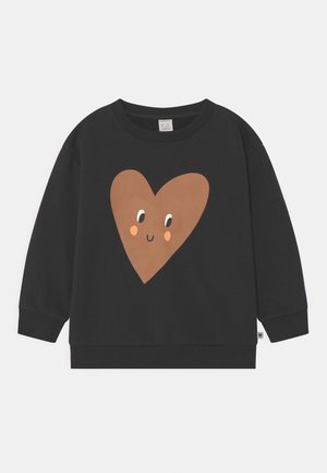 Schwarzer Sweatshirt mit langen Ärmeln und einem großen braunen Herz in der Mitte auf der Vorderseite, das Augen, rosige Wangen und ein Lächeln zeigt.