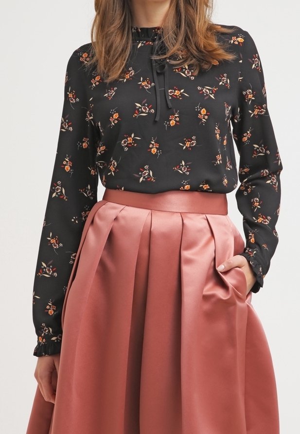 Svart blus med blommönster, samlad halsringning och långa ärmar, matchad med en rosa satin A-linjeformad kjol med veck och midjeband.
