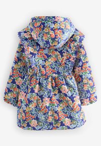 Krāsains ziedu raksta lietusmētelis ar zilu fona krāsu, ar viļņotu kapuci, elastīgu jostasvietu un garām pūkainām piedurknēm. Ūdensnecaurlaidīga auduma.