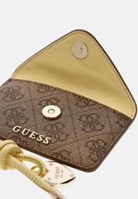 Bruine portemonnee van imitatieleren met patroon en een geel interieur, voorzien van een gouden drukknoopsluiting en een gouden logo-accent.