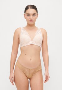 Bralet din dantelă roz deschis cu margini ondulate și o fundiță decorativă în centru. Chiloți din dantelă bej asortați, cu un model floral și o piatră prețioasă în centru.