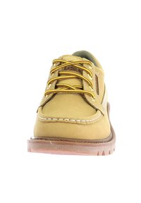 Zapato de cuero amarillo con punta redondeada, costuras en contraste en color marrón y cordones dorados. Presenta una suela de goma marrón con un patrón de tracción.