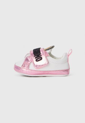 Zapatilla blanca con acentos metálicos en rosa y una correa de Velcro negra. Presenta una puntera redondeada y una lengüeta en la parte posterior para facilitar el calzado.