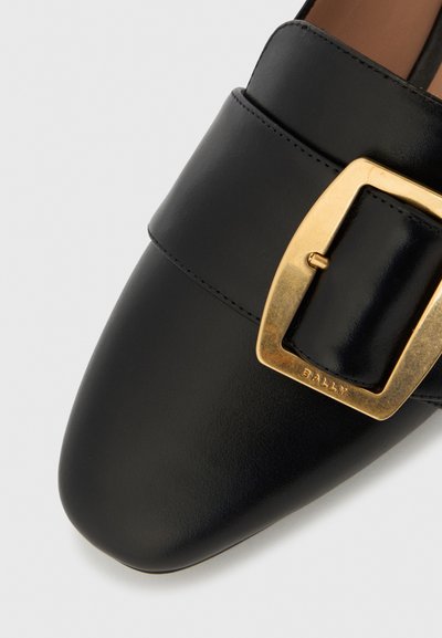 Μαύρο δερμάτινο παπούτσι με τετράγωνο χρυσό πόρπη και μυτερή μύτη. Ομαλή υφή με ελάχιστες ραφές.