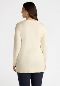 Langärmliger, cremiger beiger Pullover mit geripptem Saum und Bündchen, der über Knopfdetails an den Ärmeln und ein schlichtes, gerades Design verfügt.