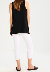 Black sleeveless top with a loose fit, paired with white cropped pants featuring side slits and black slip-on sandals.