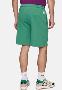 Groene katoenen shorts in een blend met een elastische tailleband, zijzakken en een klein Fila-logo op de achterkant, gecombineerd met witte sokken en sneakers.