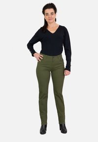 Top negro de manga larga con cuello en V combinado con pantalones ajustados en color verde oliva. Los pantalones tienen cierre de botón y bolsillos delanteros. Botines negros hasta el tobillo completan el look.