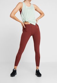 Top de malla verde menta anudado en la cintura, combinado con leggings color burdeos con bolsillos laterales y costuras geométricas, usado con zapatillas negras.