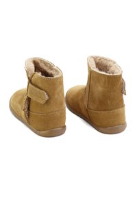 Botines de ante marrón claro con un suave forro de piel, punta redondeada y cierre de Velcro lateral. Suela de goma plana, diseño aerodinámico.