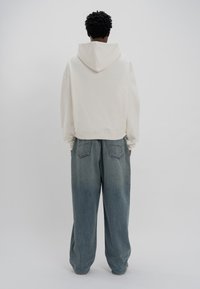 Hoodie court beige clair avec un col haut et une capuche, associé à un pantalon en denim bleu délavé ample avec des poches arrière.