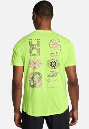 Homme portant un T-shirt vert néon avec des motifs géométriques et textuels noirs et roses dans le dos, incluant "Under Armour" et "Keep Your Mind on Track."