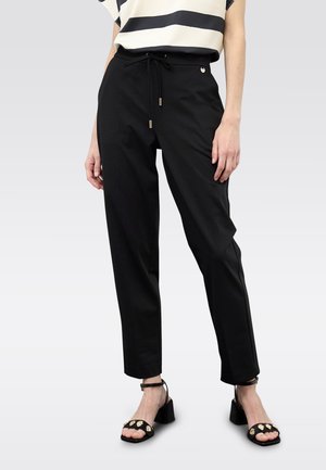 Pantalones negros a medida con cintura de cordón, que presentan una textura suave y un diseño de pierna cónica. Combinados con tacones negros de tiras.