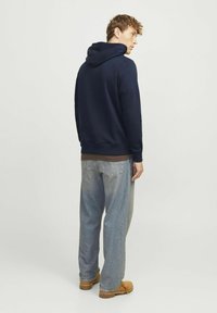 Hoodie bleu marine avec cordon de serrage ajustable, poignets et taille côtelés, associé à un jean clair, ample, et des chaussures beiges.