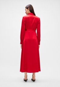 Czerwona satynowa sukienka midi z długimi rękawami i dopasowanym kołnierzykiem, z paskiem w talii i zwiewnym dołem. Gładka tekstura i elegancki design.