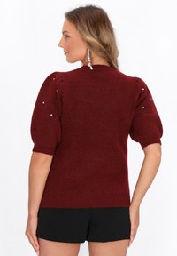 Bordeaux strikket sweater med pufærmer, der har perle detaljer på skuldrene og en ribbet kant. Blød tekstur og tætsiddende design.