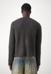 Gray fuzzy sweater with long sleeves, crew neck, and a slightly cropped hem, worn over light blue, faded jeans with decorative stitching.