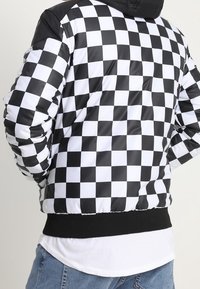 Giacca puffer a scacchi bianco e nero con cappuccio, vita elastica e una texture elegante simile alla satinata, con maniche contrastanti.