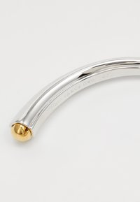Mango de metal plateado curvado con una superficie lisa y un extremo esférico dorado, que presenta grabado "kate spade new york".