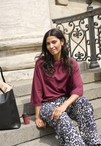 Top oversize color mogano, pantaloni a gamba larga con stampa leopardata blu e crema, borsa tote nera, tazza da caffè, seduta su gradini di pietra.