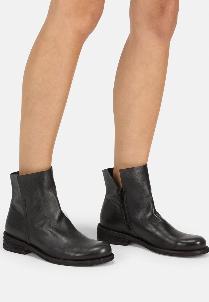 Bottes cheville en cuir noir à texture lisse, fermeture éclair latérale et talon légèrement surélevé. Caractérisées par un design minimaliste et une tige découpée.