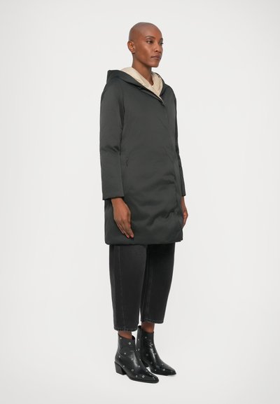 Giacca a vento nera con cappuccio e fodera beige, dotata di chiusura con zip e tasche laterali. Indossata con pantaloni neri a vita alta e stivaletti con borchie.
