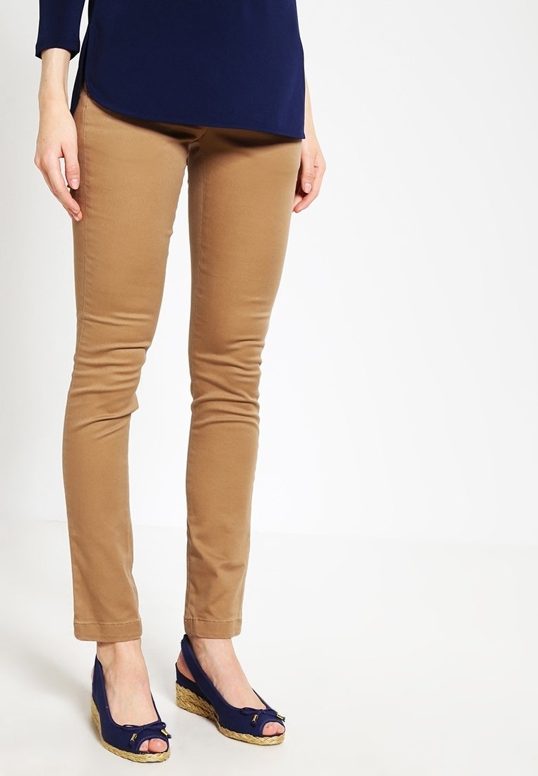 Femme portant un pantalon tan ajusté et des sandales compensées bleu marine à bouts ouverts devant un fond blanc uni.