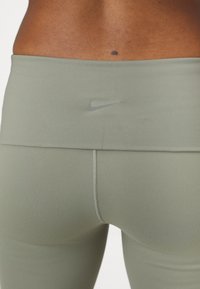 Leggings verde oliva con una textura suave, cintura alta y un logotipo gris minimalista de Nike en la parte trasera, con costuras en contraste.