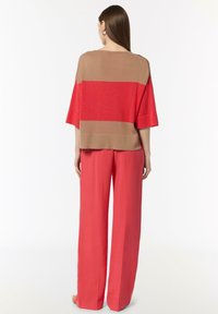 Czerwono-beżowa bluzka w paski z szerokimi rękawami, połączona z zwiewnymi czerwonymi spodniami. Tkanina wygląda na gładką o lekkiej fakturze.