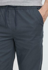 Dark navy, textured jogger pants with an elastic waistband and drawstring. Side pockets visible at the waist area.