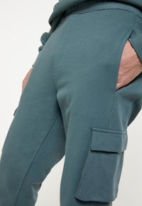 Comfortabele cargobroeken van zacht teal stof, met zijzakken en gestikte accenten, een ontspannen pasvorm en een elastische tailleband.