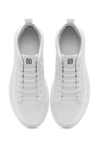 Sneakers bianchi con tomaia in pelle liscia, lacci elastici e suola in gomma piatta. Presentano un logo vicino alla linguetta e un tassello sul tallone.