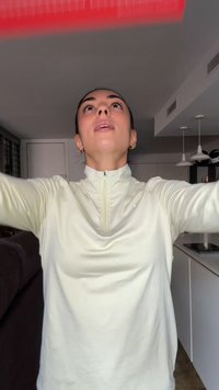 Haut de sport zippé jaune clair avec des manches longues, texture lisse et légère brillance, porté par une personne qui tend le bras vers le haut.